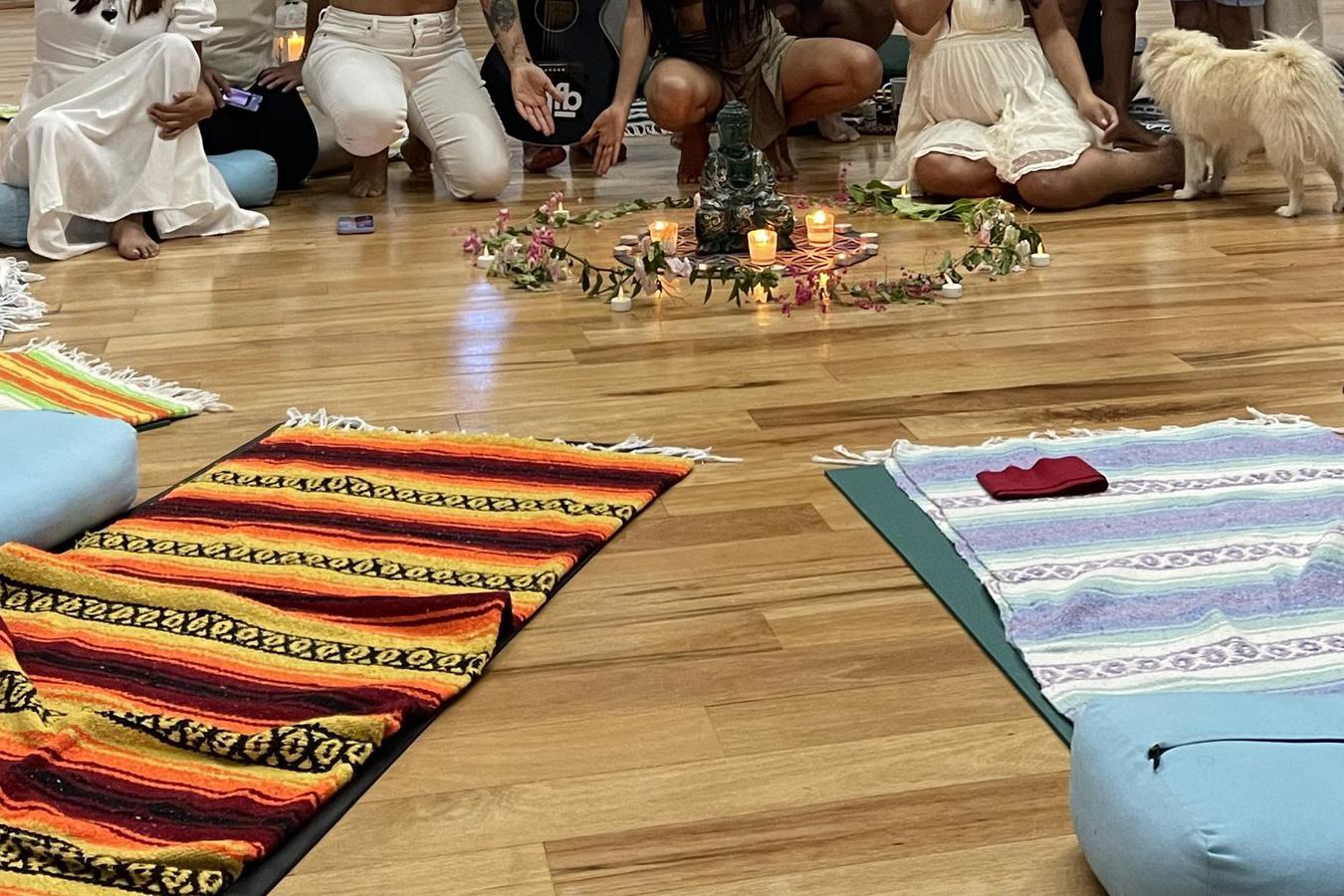 Un grupo sonriente, casi todo de blanco, reunido con un músico con guitarra alrededor de un altar de velas y flores bajo un techo de palma.