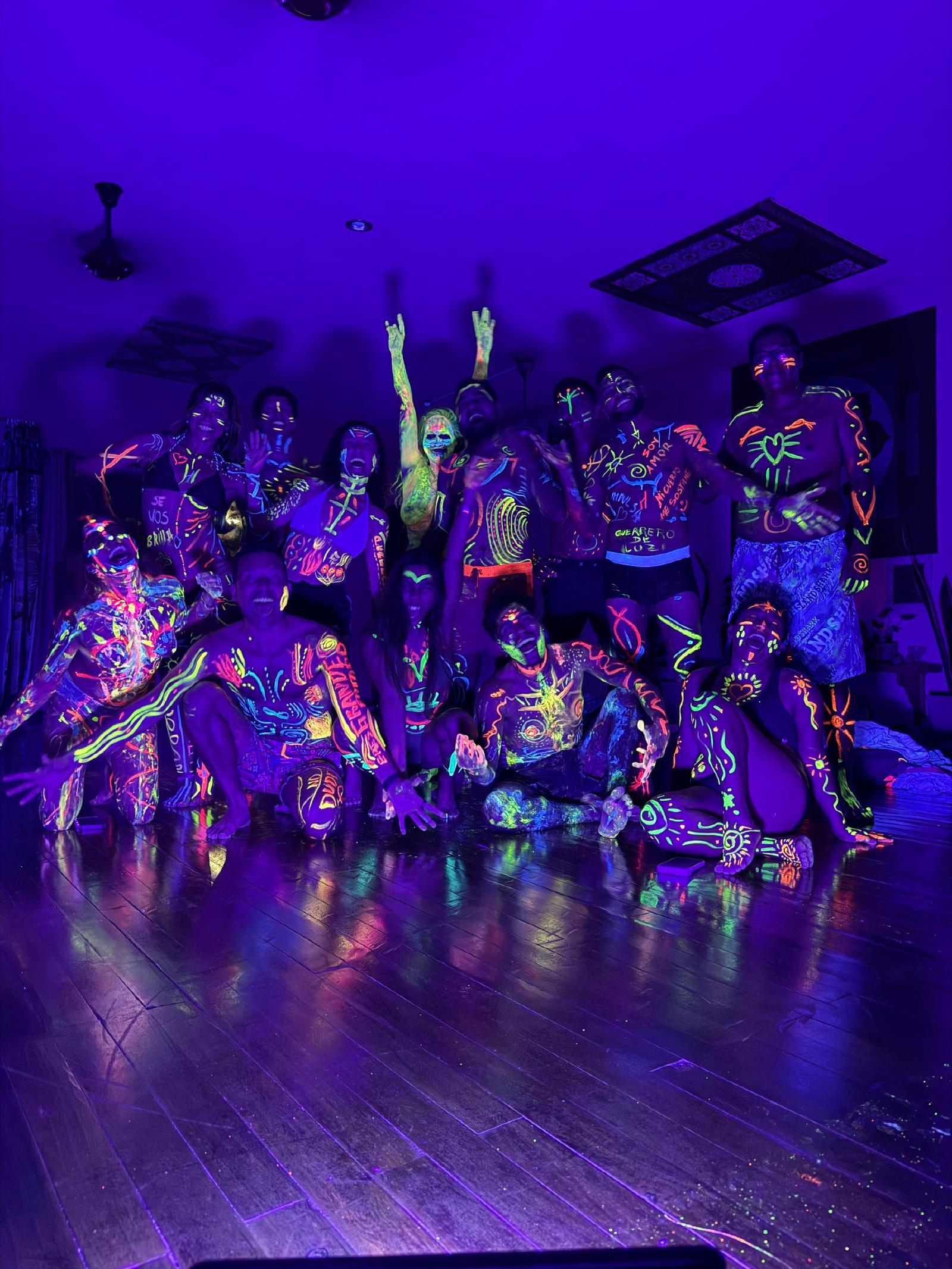 Un grupo con el cuerpo pintado con trazos, corazones y palabras fluorescentes, como «Soy amor» y «Guerrero de luz», brilla bajo luz ultravioleta.