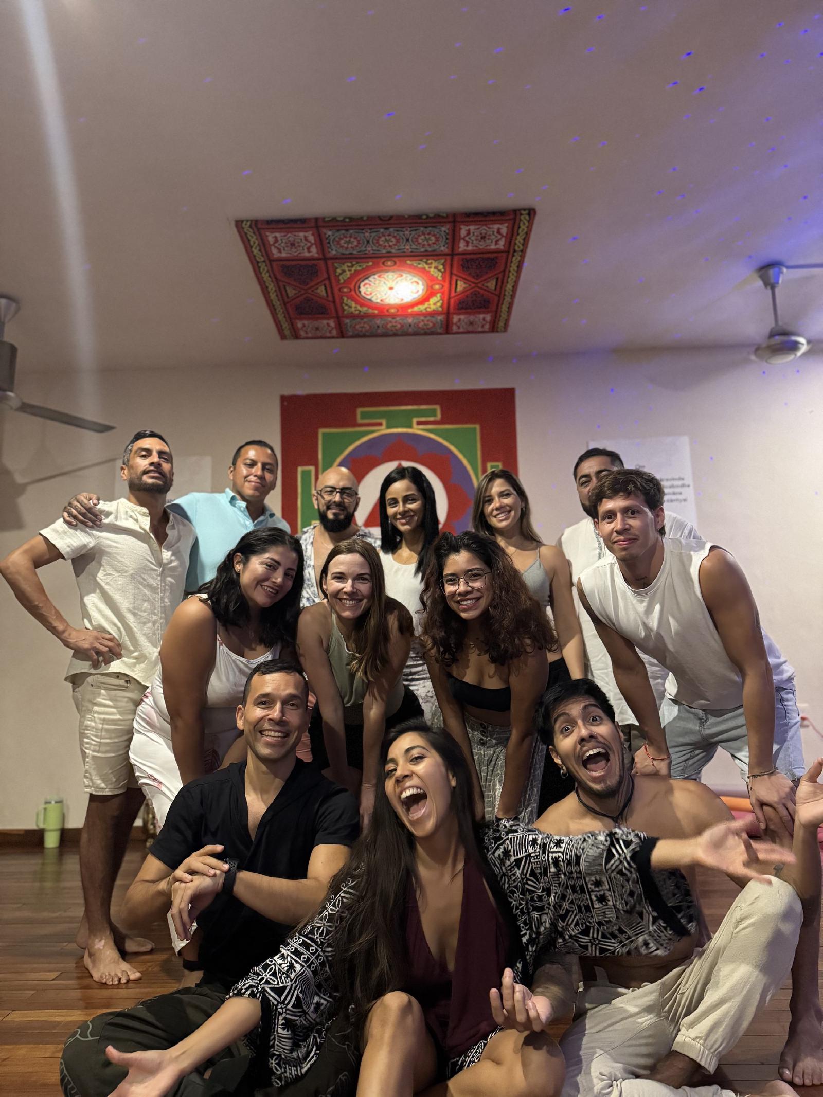 Foto de grupo alegre de hombres y mujeres, muchos de blanco, en un salón con yantra pintado y luces azules proyectadas en el techo.