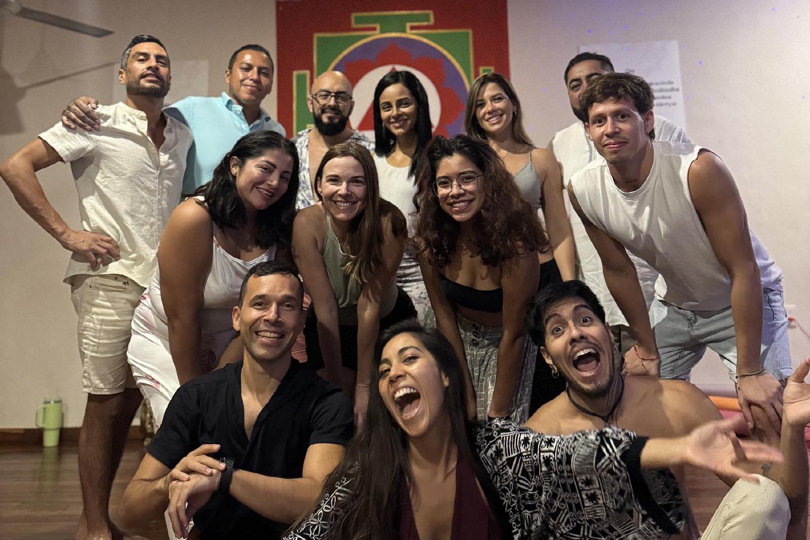 Foto de grupo alegre de hombres y mujeres, muchos de blanco, en un salón con yantra pintado y luces azules proyectadas en el techo.