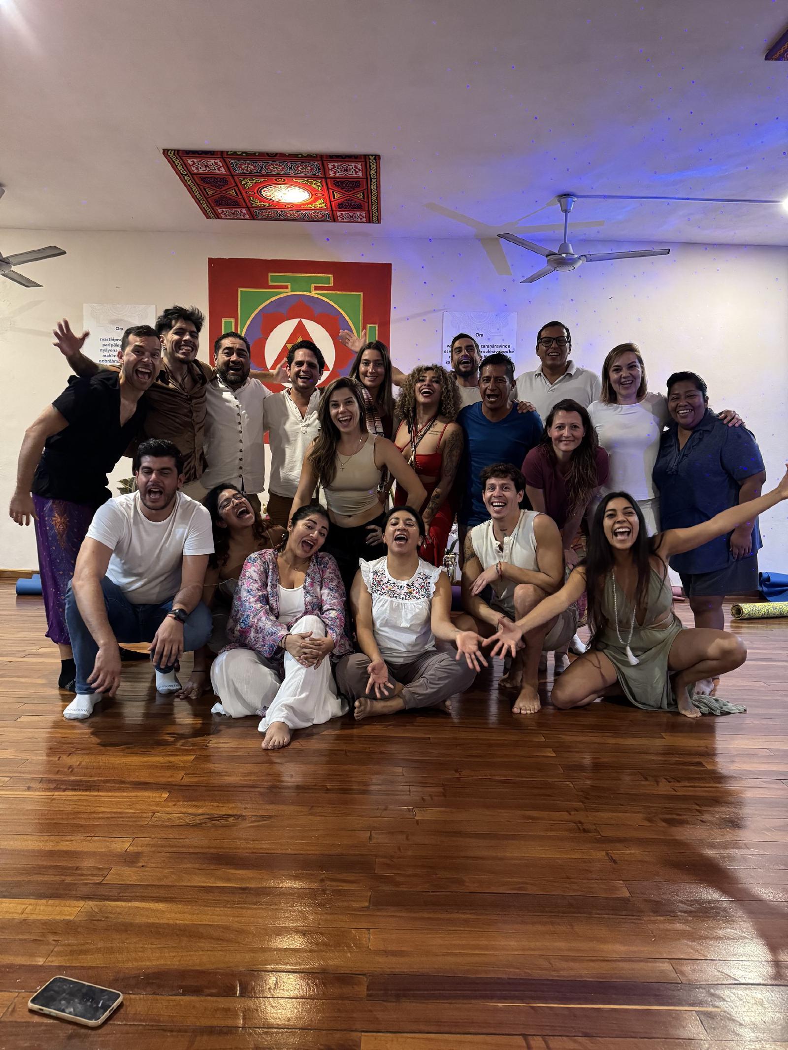 Foto de grupo de hombres y mujeres riendo con expresiones exageradas en un salón con yantra pintado, luces azules y piso de madera brillante.