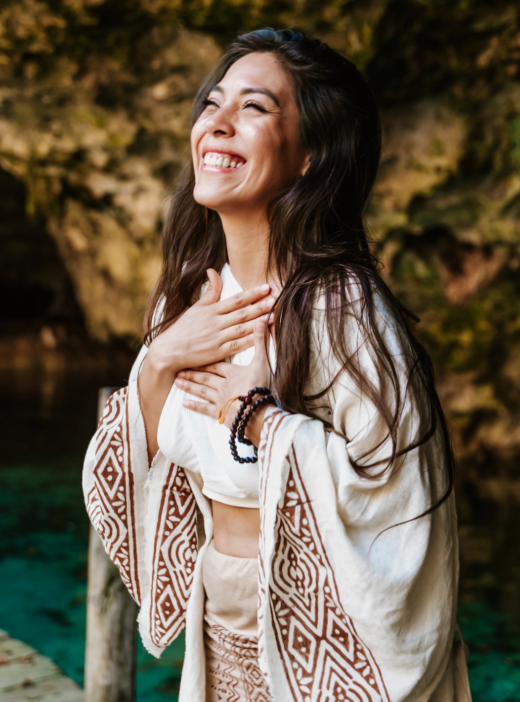 La Dra. Pamela Corona riendo con una mano en el corazón, junto a un cenote