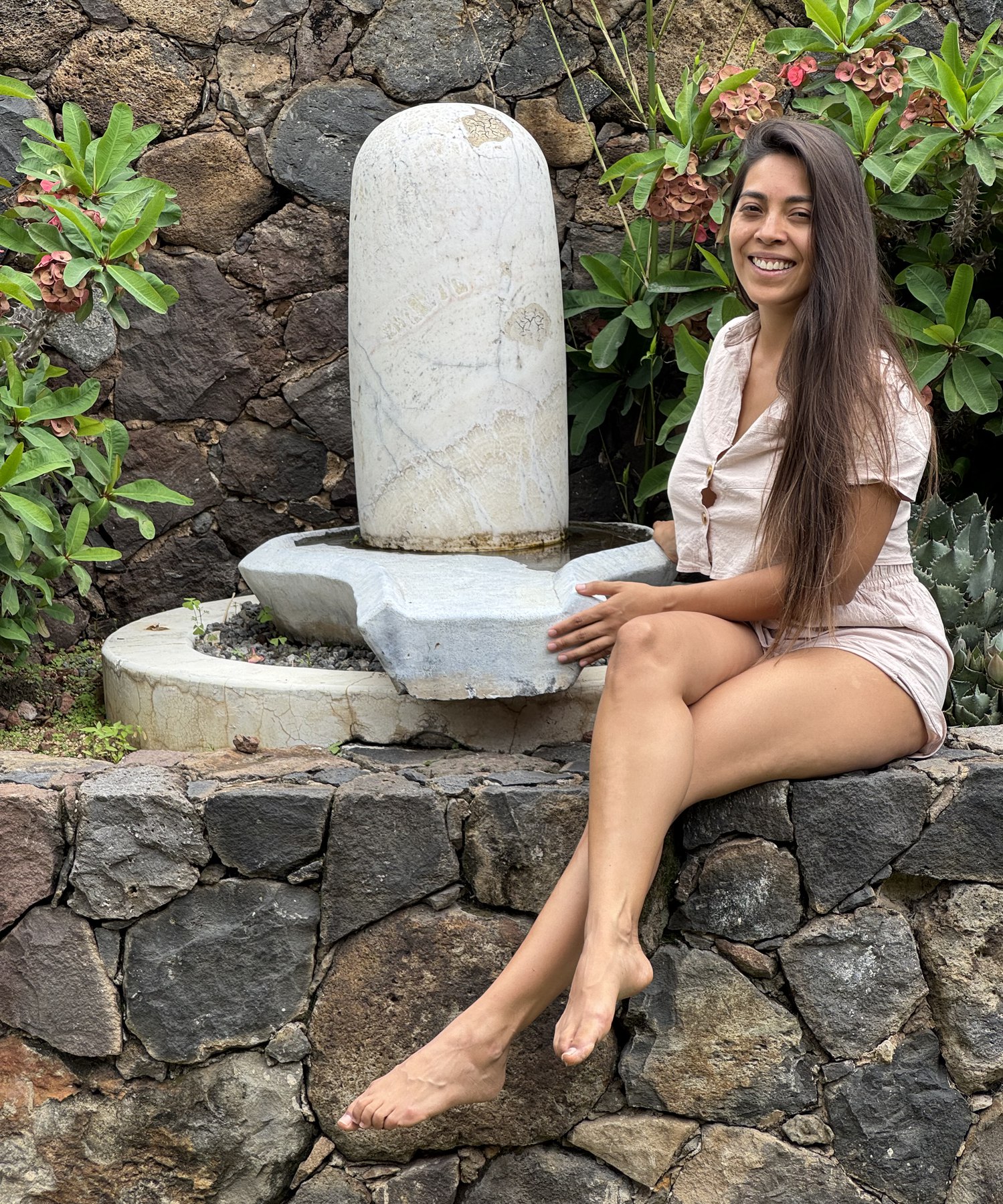 La Dra. Pamela Corona sentada junto a un lingam de piedra en un jardín