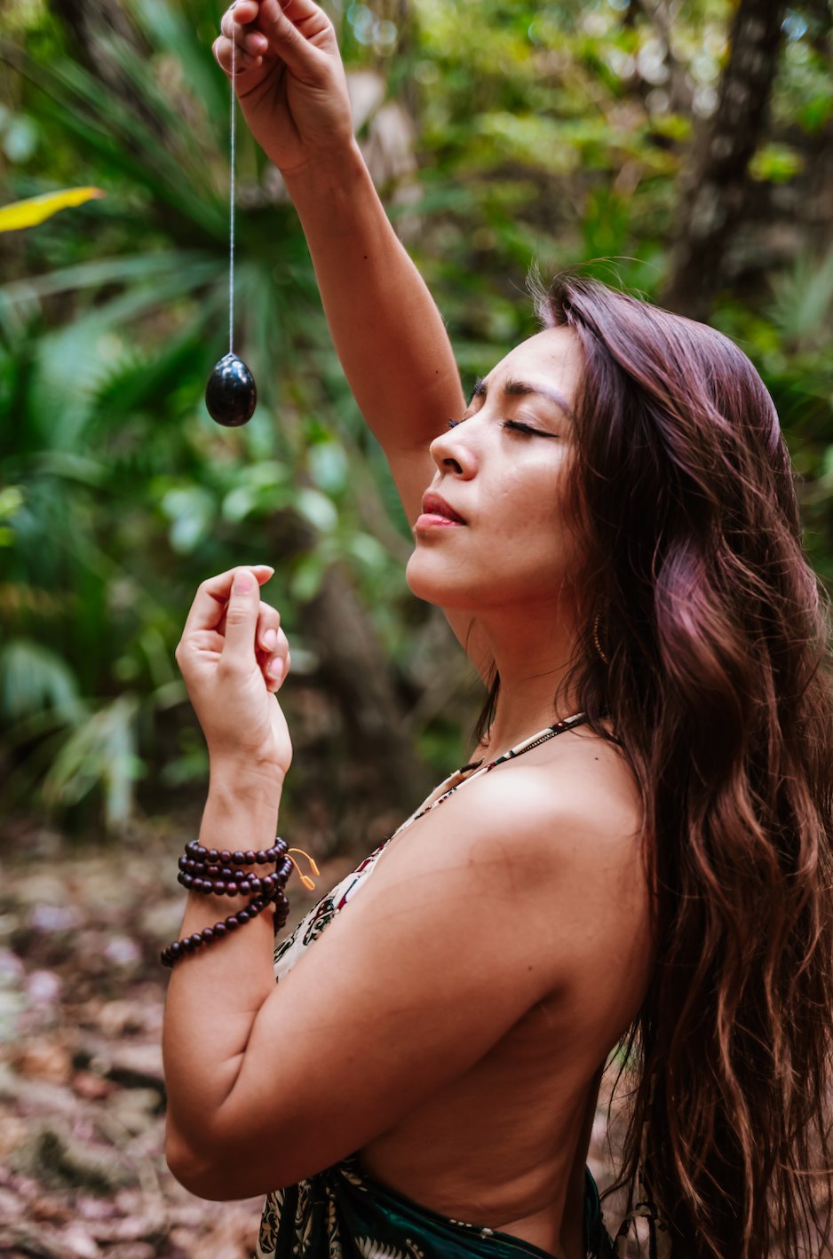 La Dra. Pamela Corona en la selva, sosteniendo un péndulo con los ojos cerrados