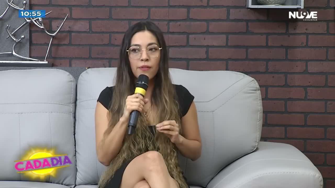 La Dra. Pamela Corona, micrófono en mano, sentada en un sillón gris frente a un muro de ladrillo en el set de Cada Día